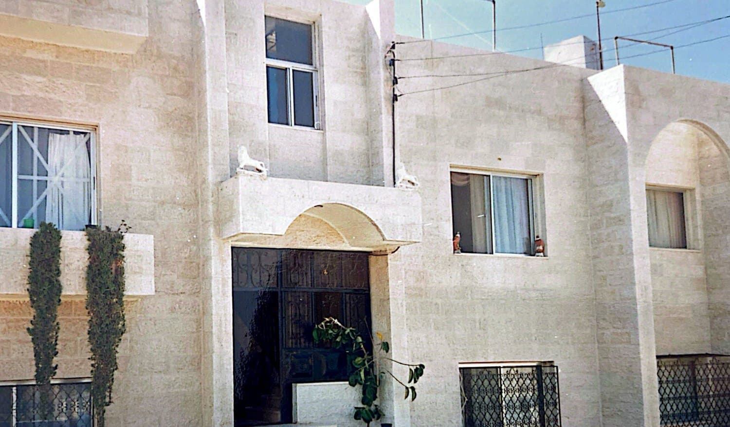 The completed two-storey cream limestone home with a central arched entrance and carved corbels, Amman