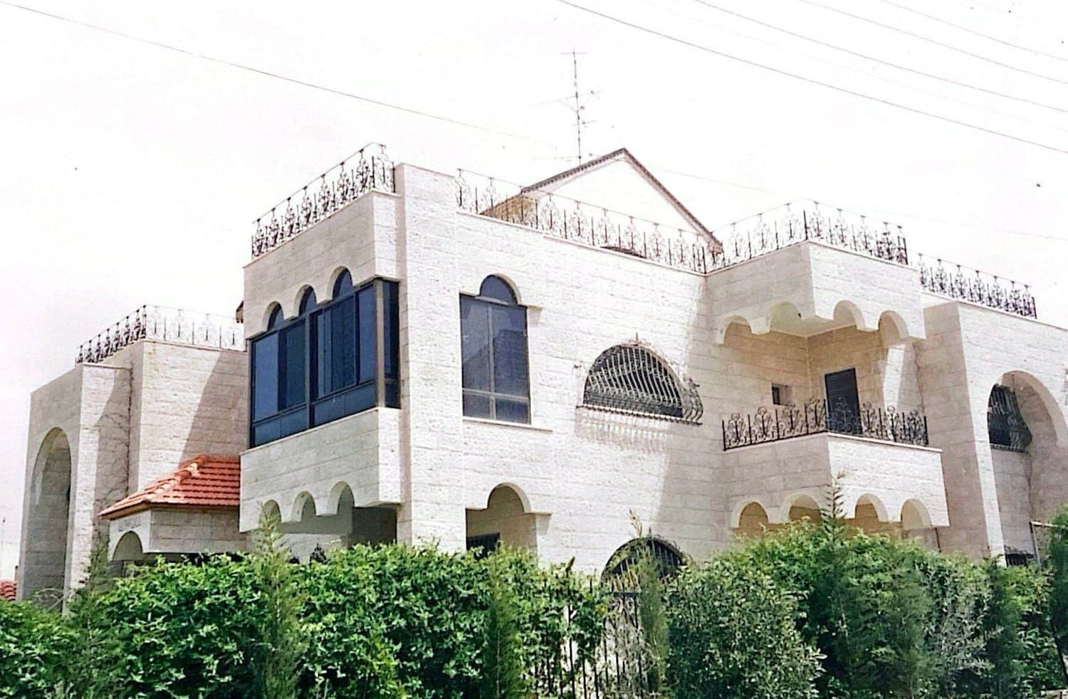 The completed cream limestone villa with arched windows, an arcaded loggia and a balustraded roof terrace, Amman